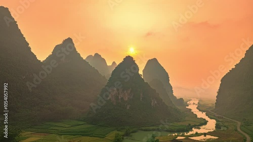 Aerial hyper lapse view of A serene sunrise over a lush valley with winding river and rice fields, framed by mist-covered karst mountains. The scene exudes tranquility and natural amazing beauty.