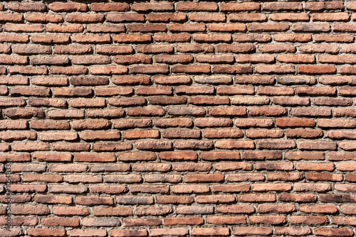 A brick wall with a brown color. The wall is made of bricks and has a rough texture