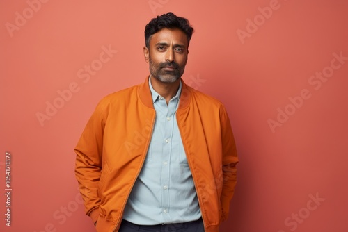 Portrait of a tender indian man in his 40s sporting a stylish varsity jacket in solid pastel color wall photo