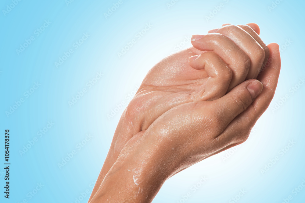 Fototapeta premium Hands applying moisturizing lotion on blue background.