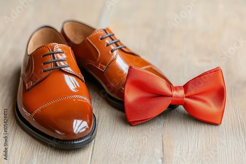 Elegant brown leather shoes and a shiny red bow tie placed on a wooden surface in preparation for a formal event photo