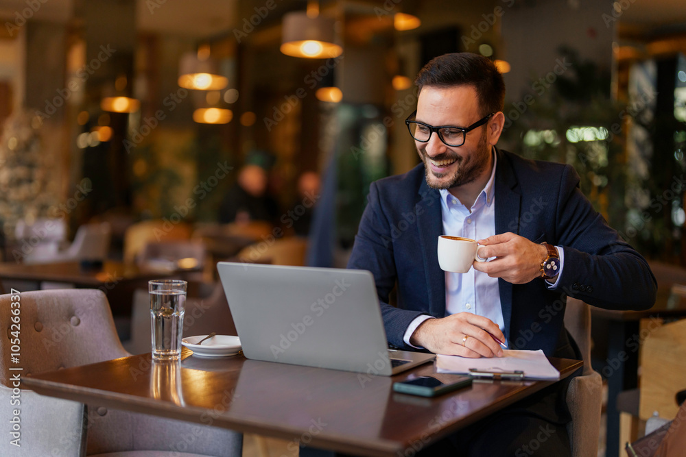 Fototapeta premium A mid-adult Caucasian man in business attire enjoys a lively video call on his laptop at a bustling modern cafe setup, with coffee and water on his table.