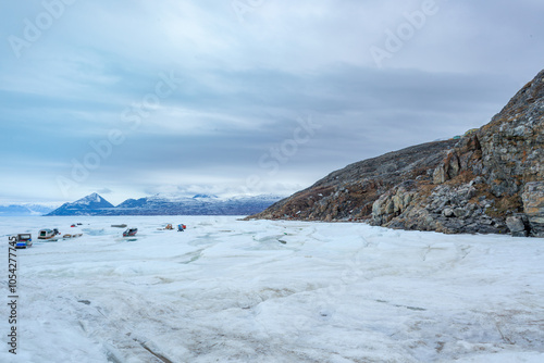 Snowmobiles and Boats on Icy Pond Inlet with Mountainous Backdrop