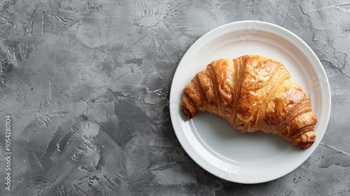 Croissant on a white plate on a gray background. The picture shows the concept of breakfast. photo