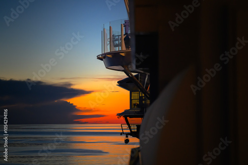 Golden sunrise hues paint the sky, casting a serene glow over the calm Atlantic waters as the cruise ship gently glides forward. A peaceful morning at sea.