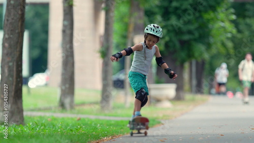 Young boy skateboarding on a pathway, momentarily losing balance as he navigates the ride. He is wearing a helmet and protective gear, focused on regaining control in active play photo