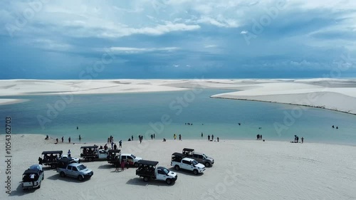 A drone reveals the vast white dunes of Lençóis Maranhenses, with shimmering lagoons nestled between the rolling sands. The sweeping aerial view captures the stunning contrast of the endle