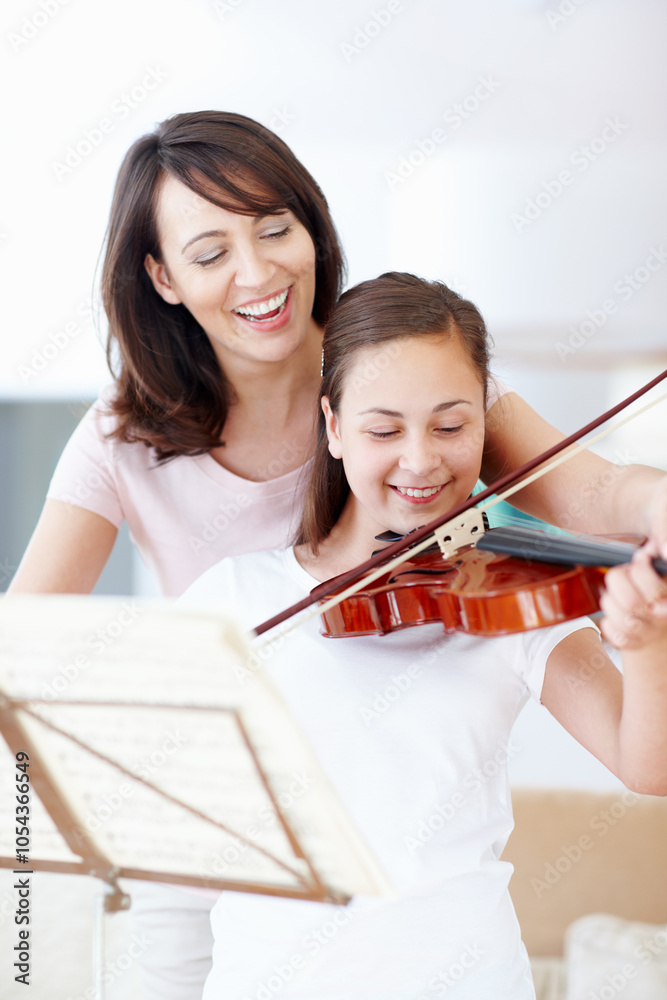Mother, violin and helping child in home with music and support for talent show or performance practice. Musician, happy and playing with teaching, love and family care in lounge with instrument Mother, violin and helping child in home with music and support for talent show or performance practice. Musician, happy and playing with teaching, love and family care in lounge with instrument