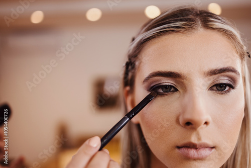 Makeup process. Professional artist applying make up on model face. Close up portrait of beautiful blonde woman in beauty salon.