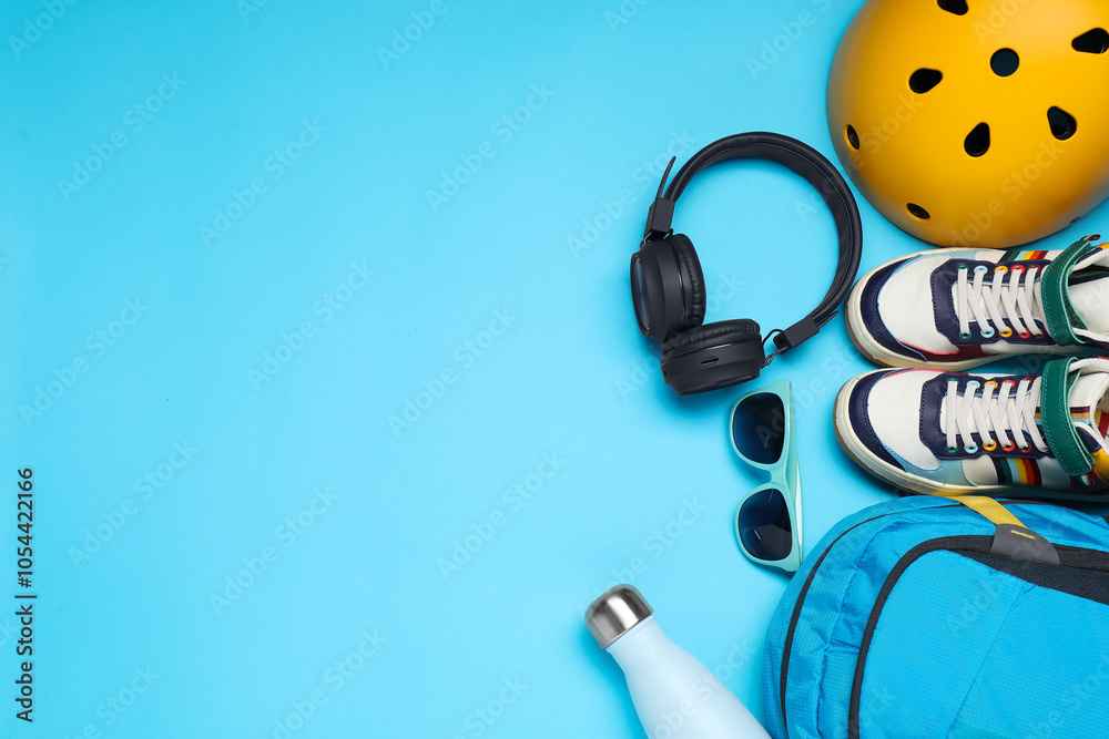 Bicycle helmet, accessories and sneakers on light blue background, flat lay. Space for text