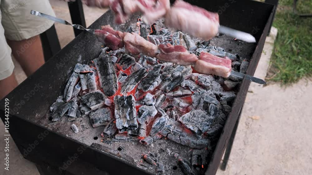 A person cooks skewered meat over hot, glowing coals in the backyard during summer. Grilling delicious skewers over glowing charcoal embers in a backyard setting. A person cooks skewered meat over hot, glowing coals in the backyard during summer. Grilling delicious skewers over glowing charcoal embers in a backyard setting.
