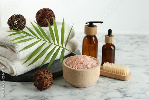 Spa treatment. Towels, sea salt, brush, bottles of cosmetic products and palm leaf on white marble table photo