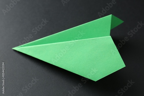 One handmade green paper plane on black background, closeup