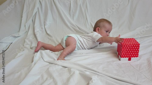 Little baby on bed reaching the present box