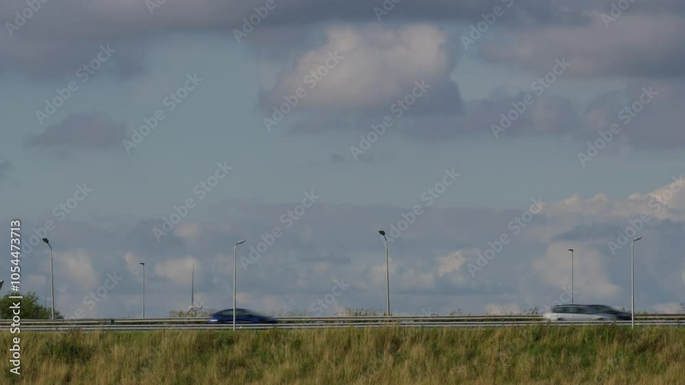 Cargo truck with a red and white cabin moving on a highway under a partly cloudy sky with street lights and grass in the foreground Cargo truck with a red and white cabin moving on a highway under a partly cloudy sky with street lights and grass in the foreground