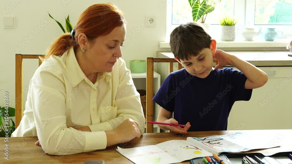 Mother and son sitting at the table and doing homework at the kitchen room Mother and son sitting at the table and doing homework at the kitchen room