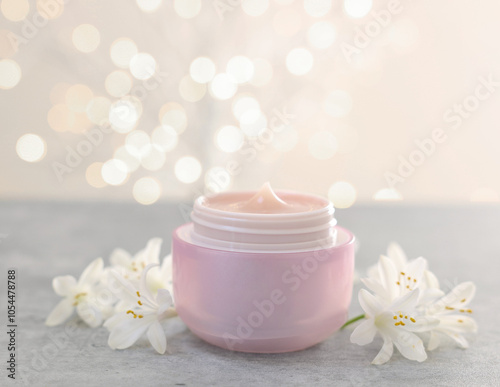 Cream in jar and beautiful jasmine flowers on grey table against light background with blurred lights, closeup. Space for text