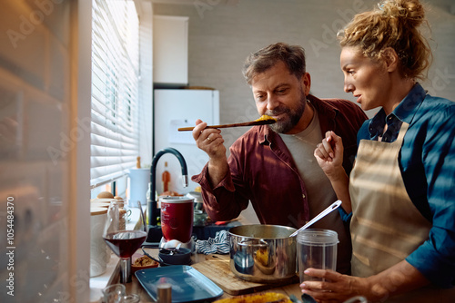 Smiling man tasting food cooked by his wife in kitchen.