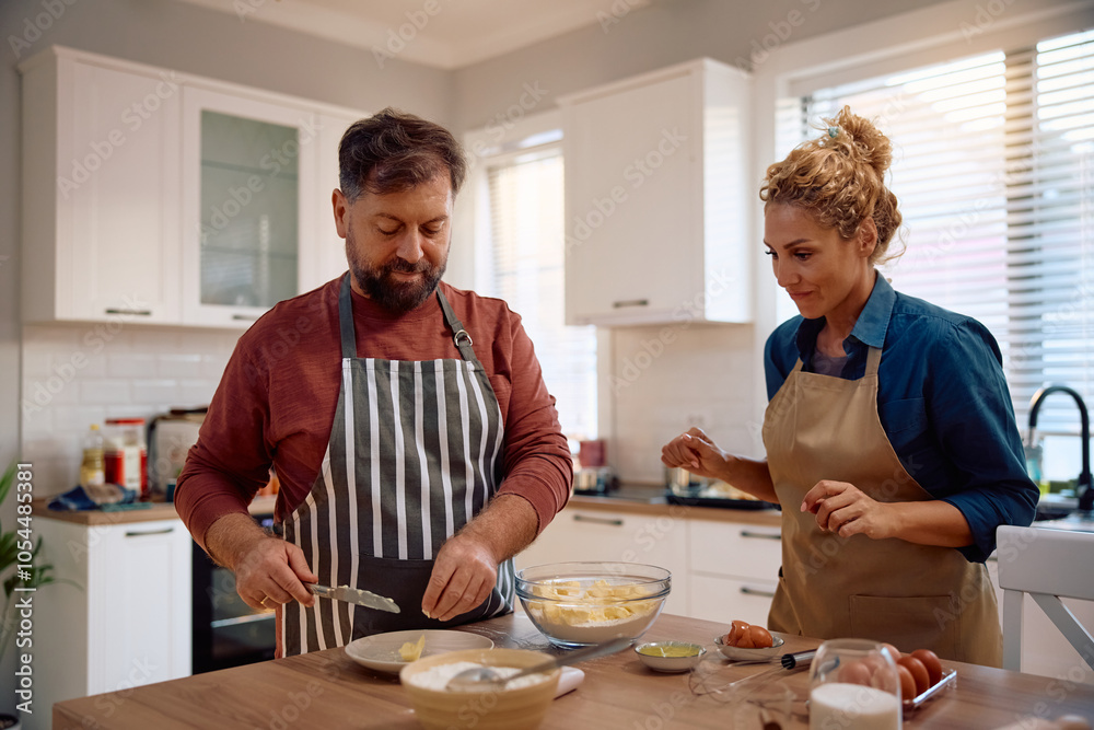 Mid adult couple baking together in kitchen.