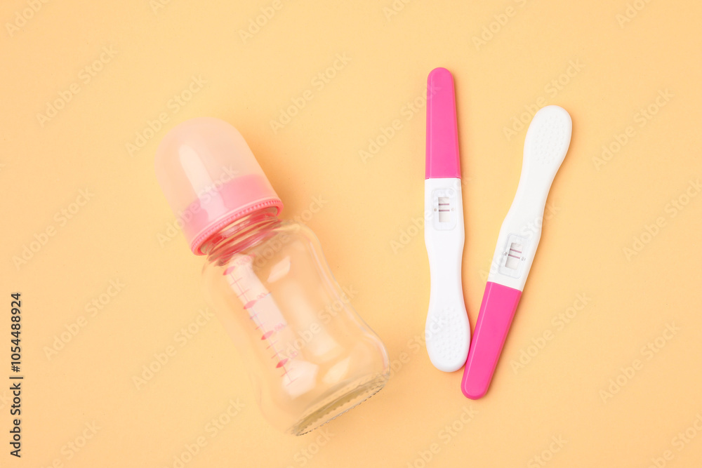 Pregnancy tests and baby bottle on pale orange background, top view Pregnancy tests and baby bottle on pale orange background, top view