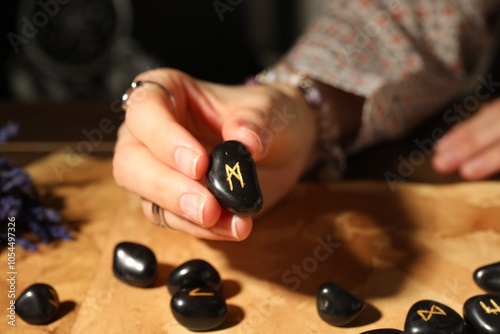 Woman with black rune Mannaz at table indoors, closeup photo