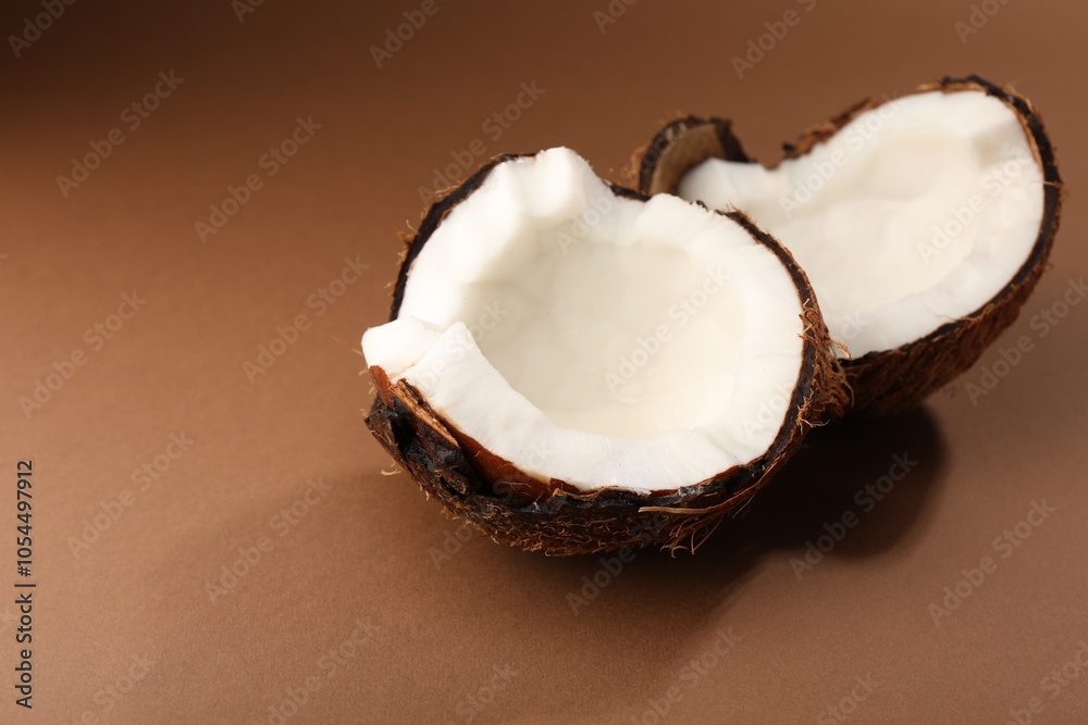 Halves of cracked coconut on brown background, closeup. Space for text Halves of cracked coconut on brown background, closeup. Space for text