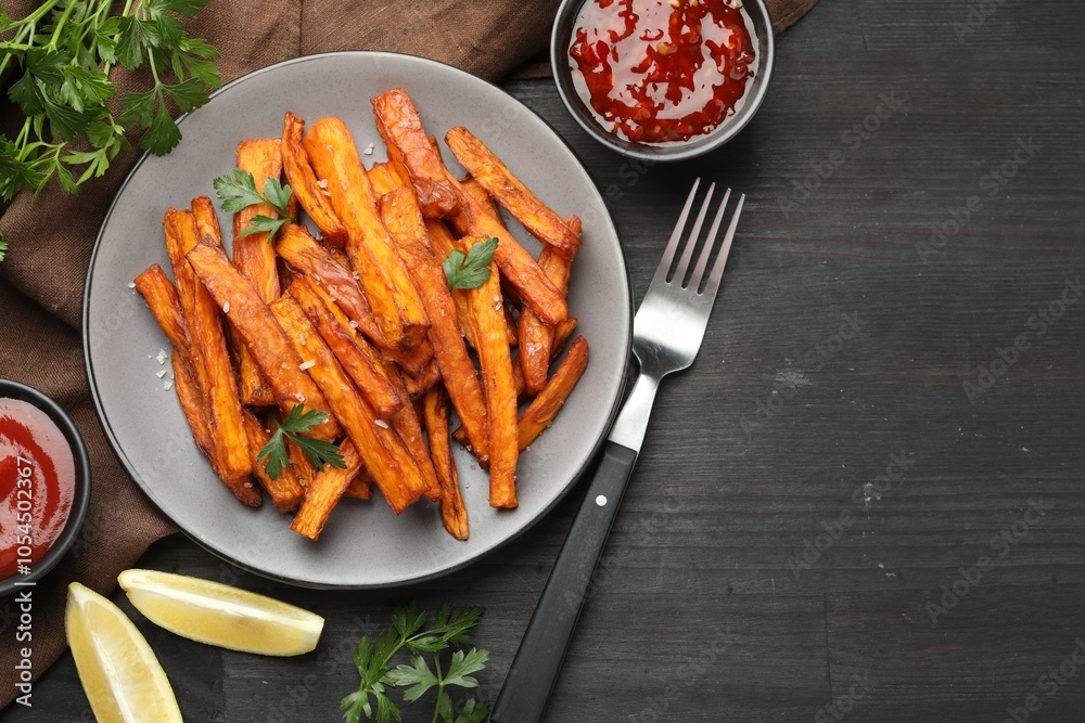 Delicious sweet potato fries with spices and sauces on black wooden table, top view. Space for text