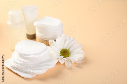 Cotton pads, cosmetic products and daisy flower on beige background, closeup. Space for text