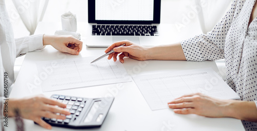 Accountant using a calculator and laptop computer for counting taxes with a client or a colleague at white desk in office. Teamwork in business audit and finance photo