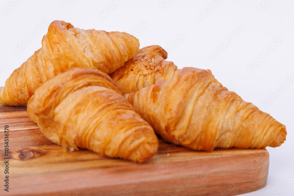Golden croissants on a wooden cutting board placed against an infinite white background, showing texture and detail in the pastry's layers
