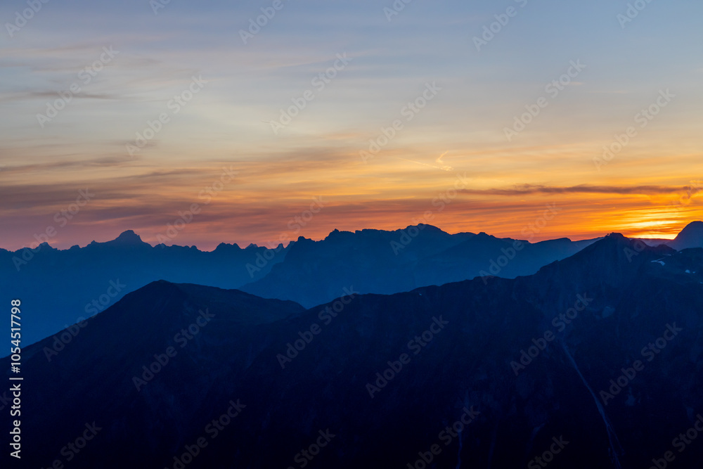 Fototapeta premium Sunset burning red and orange sky above the snow summits and rocky peaks of the Alps. Beautiful mountain sunset and sunrise in Chamonix valley on the ascent to Montblanc