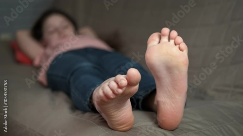Child leisure with bare feet on sofa. A little girl have free time and lie with bare feet on the sofa.