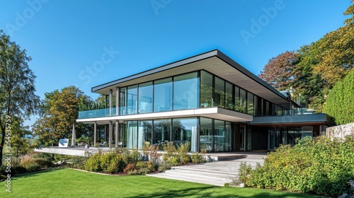 Modern glass house with a landscaped garden and clear blue sky.