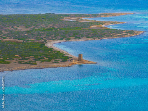 An aerial view captures a historical tower on Sardinia's coast, surrounded by Mediterranean waters with blue gradients and low vegetation. photo