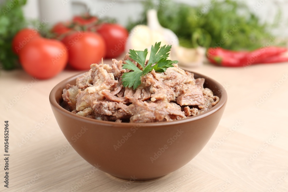 Canned meat with parsley in bowl on wooden table, closeup