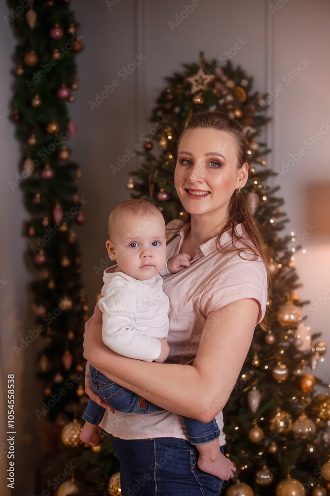 Mom holding baby in her arms against the background of a Christmas tree Mom holding baby in her arms against the background of a Christmas tree
