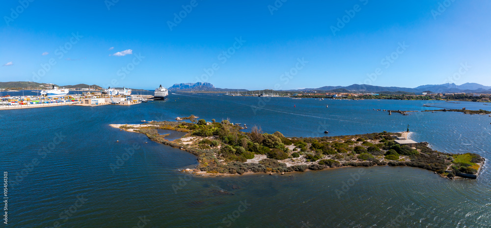 Fototapeta premium Aerial view of Olbia port in Sardinia, featuring cruise ships, a lush island, and the Mediterranean Sea, with rugged mountains in the background.