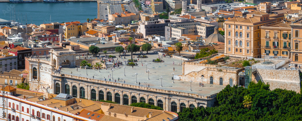 Fototapeta premium Aerial view of Cagliari, Sardinia, highlighting Bastione di Saint Remy with its terrace and arches. Colorful buildings and a bustling harbor are visible.