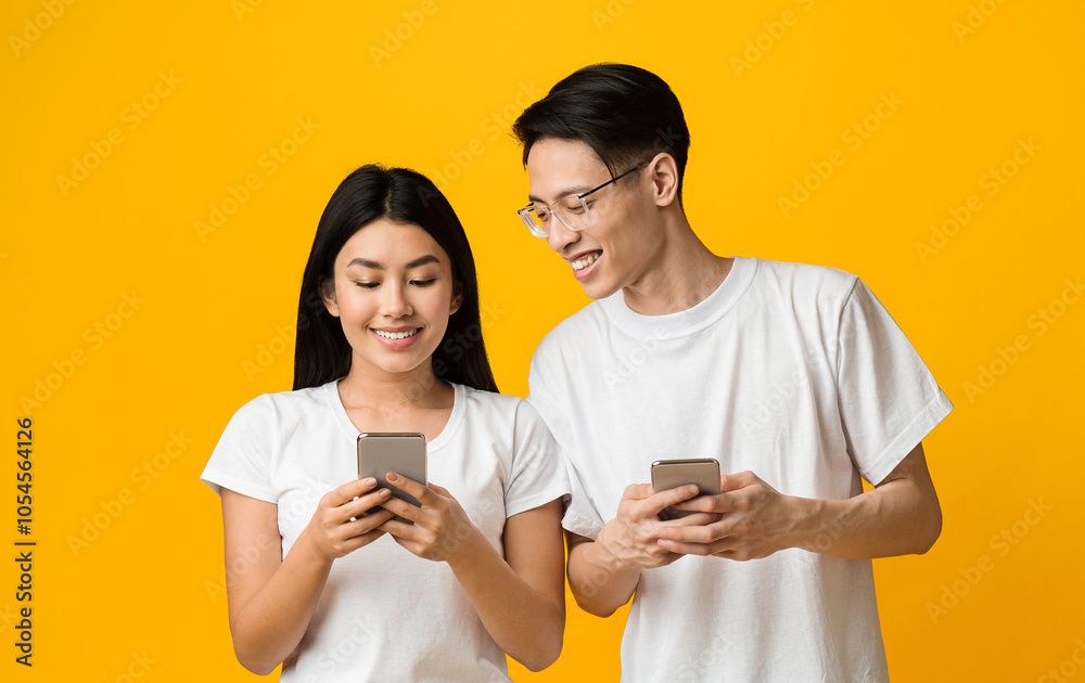 Smiling asian guy looking at his girlfriend smartphone while she is chatting with someone, trust in couple concept Smiling asian guy looking at his girlfriend smartphone while she is chatting with someone, trust in couple concept