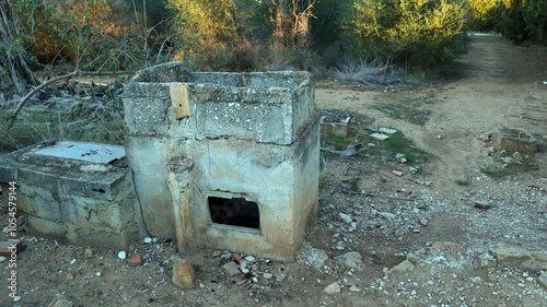 Abandoned stove remnants from a destroyed house in a rural area, surrounded by overgrown foliage and debris photo