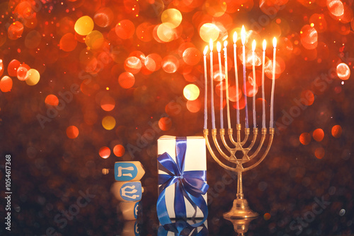 Menorah with burning candles, dreidels and gift for Hanukkah celebration on dark background