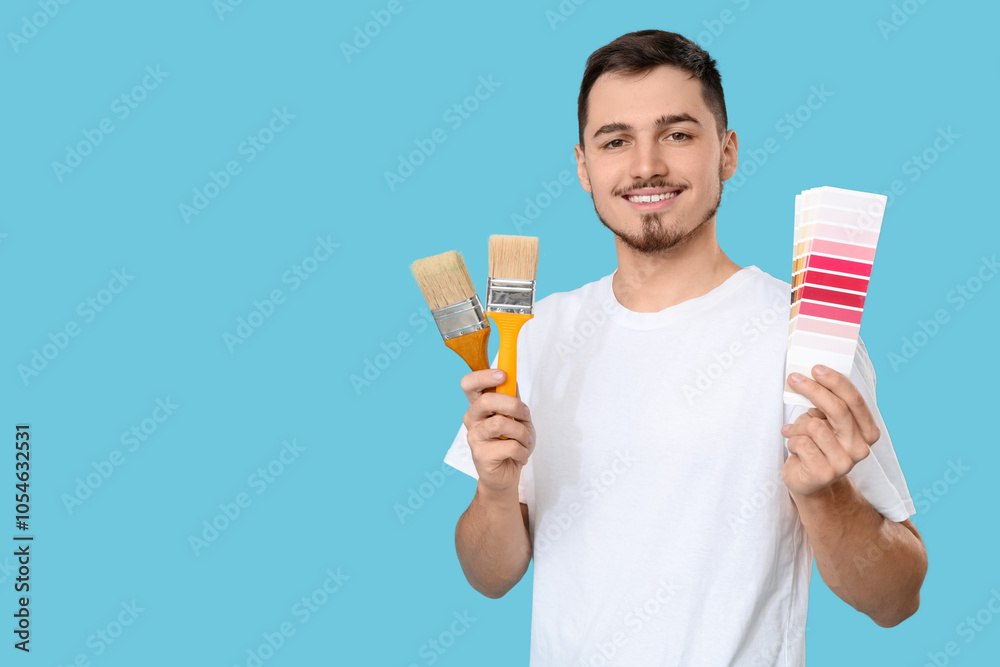 Young man with color palettes and paint brushes on blue background Young man with color palettes and paint brushes on blue background