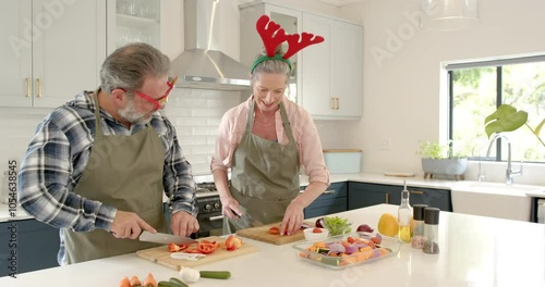 At Christmas, Mature couple wearing festive accessories preparing vegetables together in kitchen photo