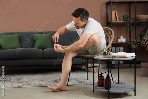 Handsome young happy man with scissors cutting cuticle and doing pedicure at home photo