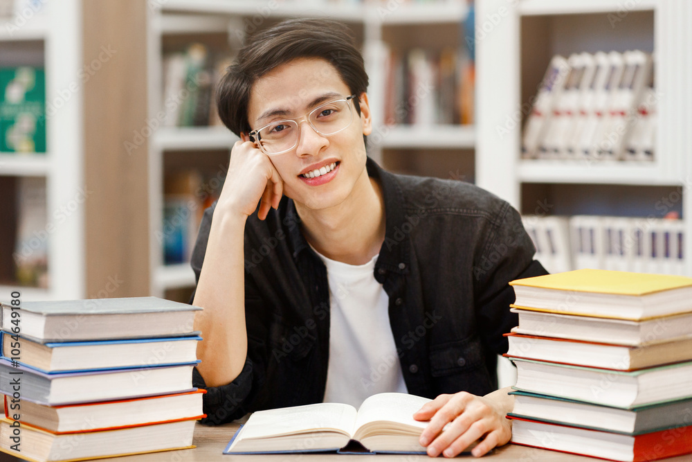 Education Concept. Cheerful asian boy sitting in library with open book, doing research, looking at camera, copyspace Education Concept. Cheerful asian boy sitting in library with open book, doing research, looking at camera, copyspace