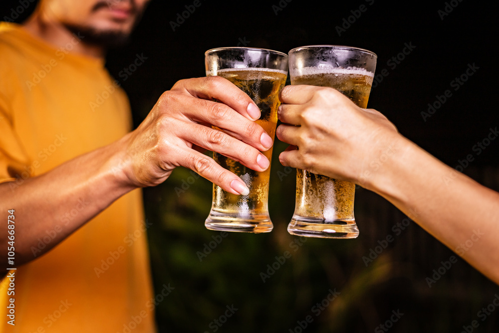A man's hand and a woman's hand hold beer glasses in a cozy, lively evening party setting. Family and friends gather under the night sky, sharing joyful moments and laughter. A man's hand and a woman's hand hold beer glasses in a cozy, lively evening party setting. Family and friends gather under the night sky, sharing joyful moments and laughter.