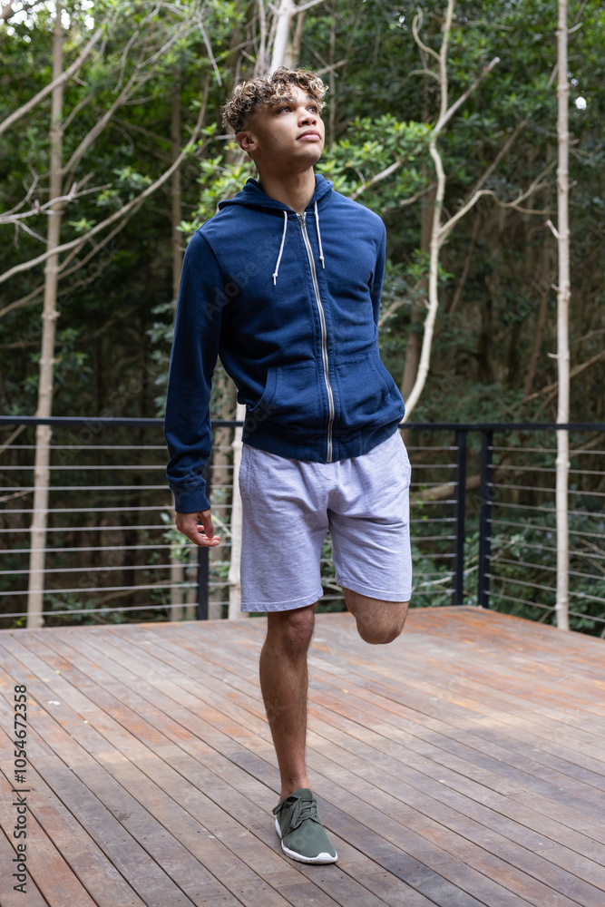 Young man in blue hoodie enjoying nature on wooden deck in forest