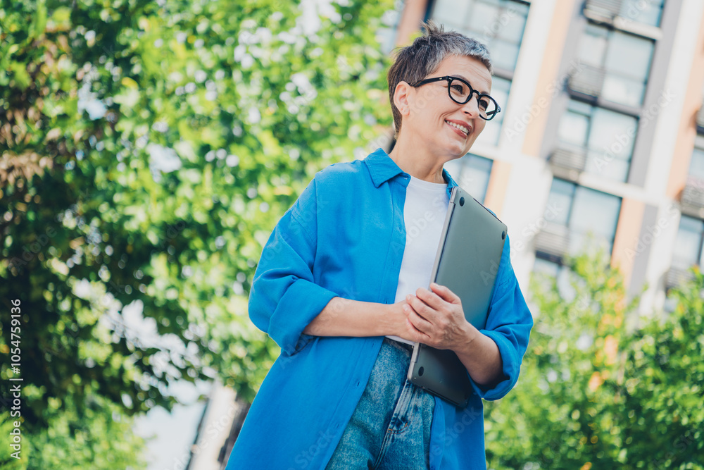 Portrait of pretty aged woman hold laptop look away wear blue shirt weekend walk city center outdoors Portrait of pretty aged woman hold laptop look away wear blue shirt weekend walk city center outdoors
