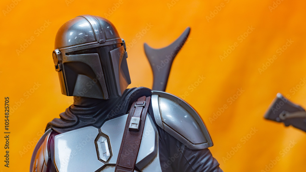 Fototapeta premium 8th Comic Con Convention In GUAYAQUIL, ECUADOR - AUG 06, 2023 - Close-up of Mandalorian figurine with detailed armor against an orange background, inspired by Star Wars. Perfect for sci-fi enthusiasts