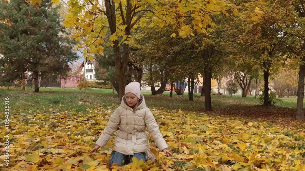 Happy teenage girl in jacket and hat pick up leaves and drop off in park. Autumn and seasons. Trees with yellow leaves. Happy teenage girl in jacket and hat pick up leaves and drop off in park. Autumn and seasons. Trees with yellow leaves.